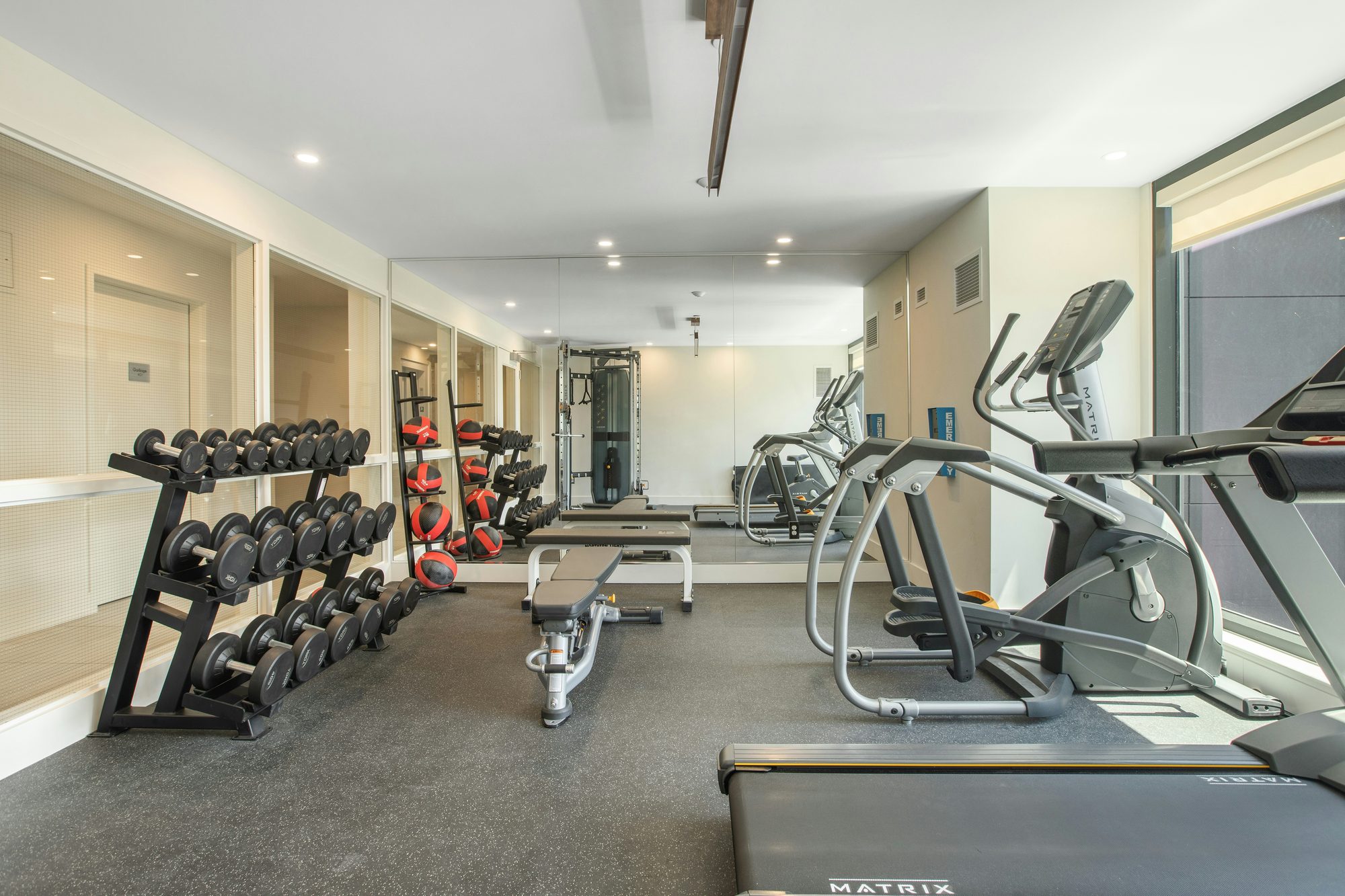 A mirrored building gym with dumbbells and cardio machines