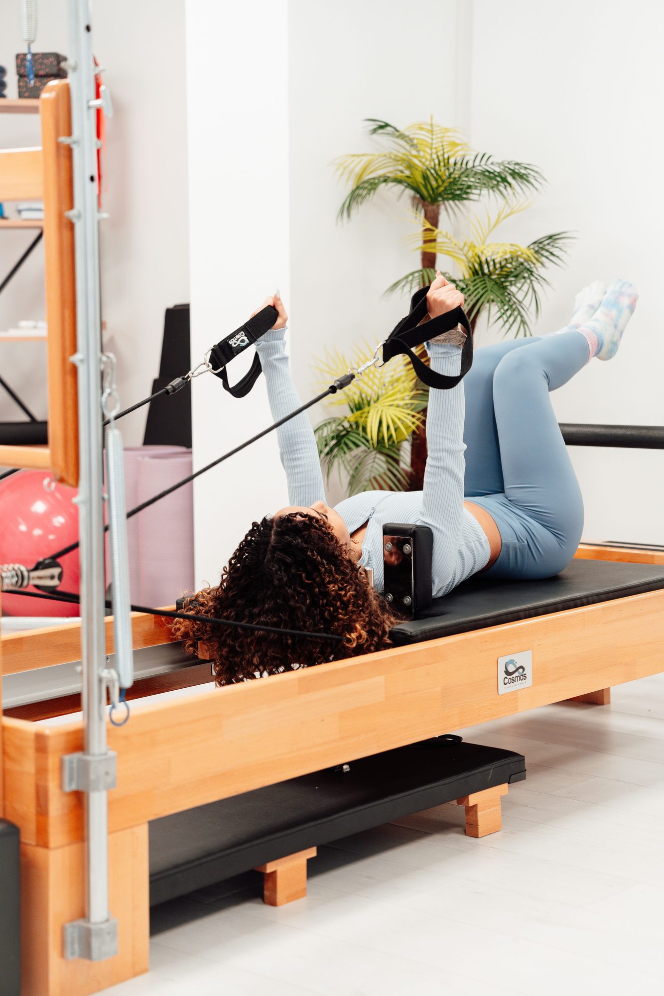 A woman lying on a reformer holding the straps overhead